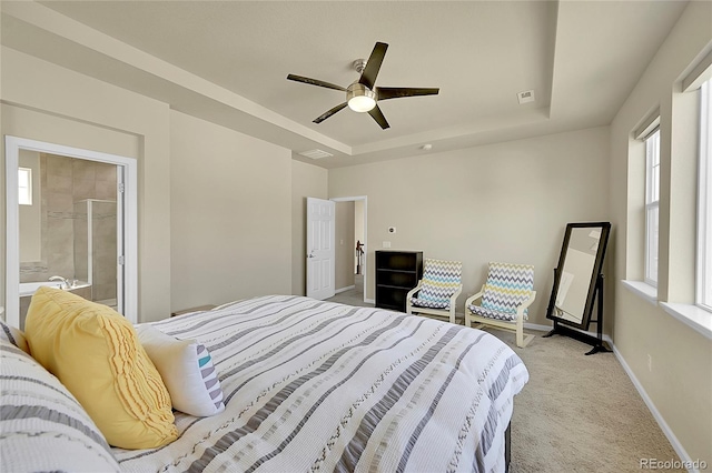 bedroom with ensuite bath, light colored carpet, a raised ceiling, and ceiling fan