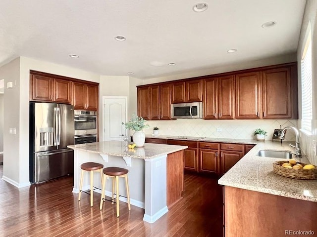 kitchen with light stone countertops, a sink, stainless steel appliances, a kitchen bar, and a center island