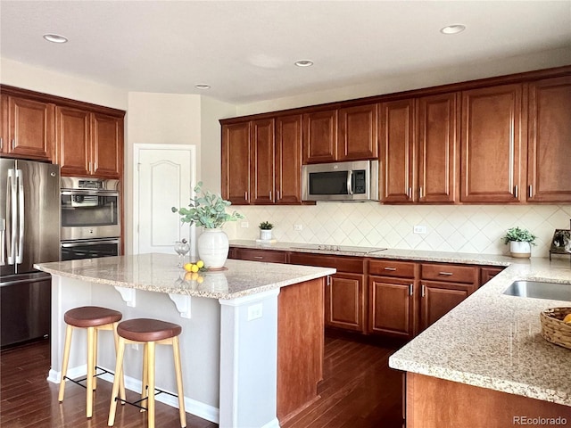 kitchen with a center island, light stone countertops, a breakfast bar, appliances with stainless steel finishes, and dark wood-style flooring