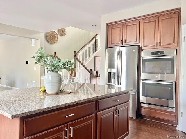 kitchen with a center island, light stone countertops, dark wood-style flooring, and stainless steel appliances