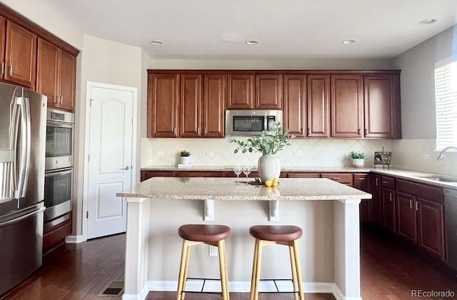 kitchen with a breakfast bar, a sink, light stone counters, a center island, and appliances with stainless steel finishes