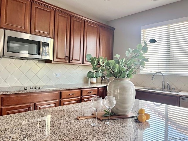 kitchen with light stone countertops, a sink, stainless steel microwave, brown cabinets, and backsplash