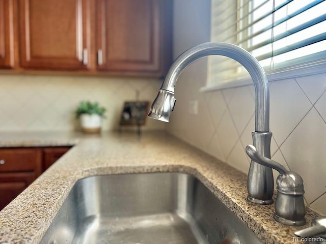 interior details with a sink, light stone counters, backsplash, and brown cabinets