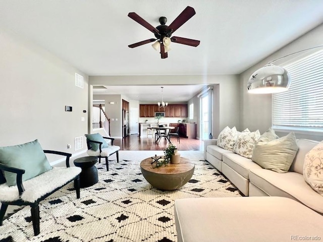 living area with visible vents, ceiling fan with notable chandelier, stairs, and wood finished floors