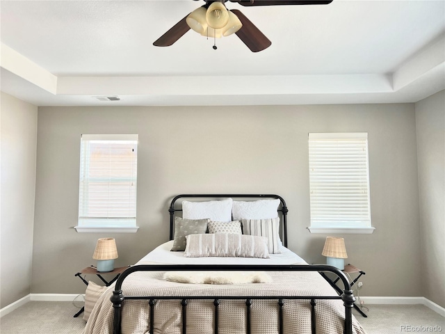 bedroom with a tray ceiling, visible vents, light carpet, and baseboards