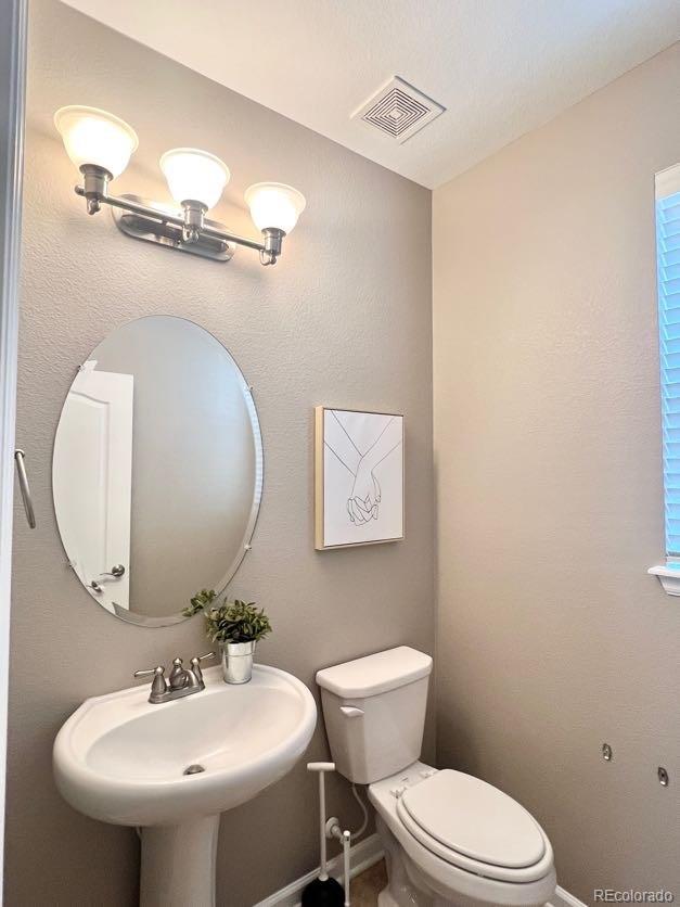 half bath with toilet, baseboards, visible vents, and a sink