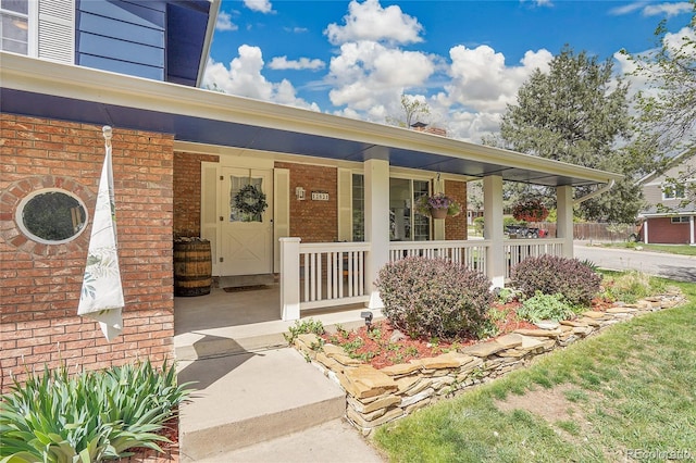 view of exterior entry featuring brick siding and a porch