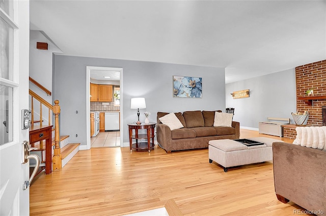 living area with light wood-style floors, baseboards, a fireplace, and stairs