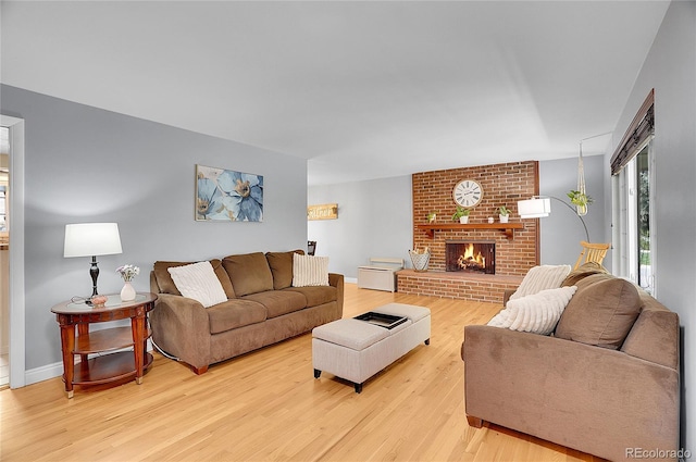 living room featuring baseboards, light wood-style flooring, and a brick fireplace
