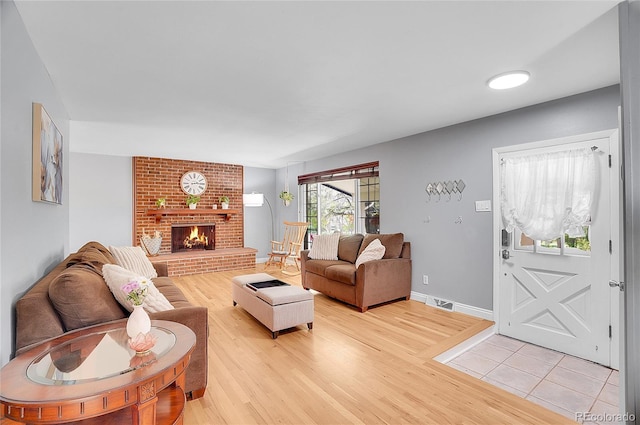 living area featuring a brick fireplace, light wood-type flooring, and visible vents