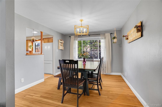 dining area with baseboards, a notable chandelier, and light wood-type flooring