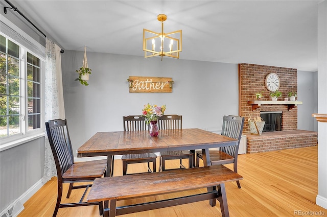 dining space with visible vents, a brick fireplace, baseboards, light wood-type flooring, and a notable chandelier
