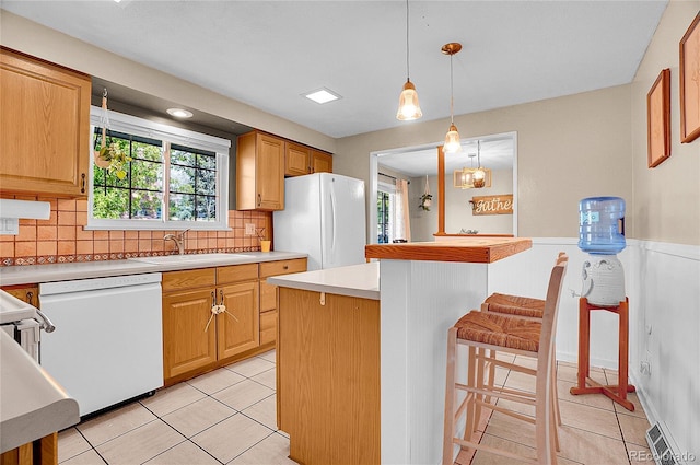 kitchen featuring a sink, white appliances, light countertops, decorative backsplash, and a kitchen bar