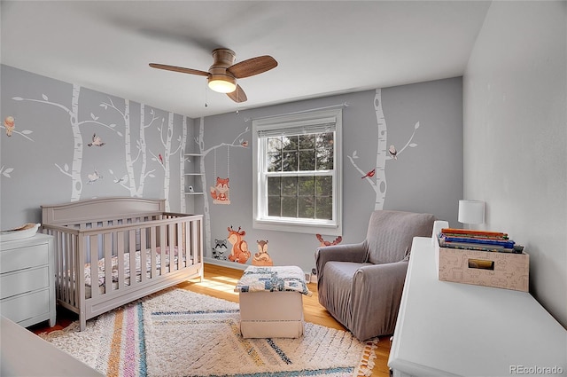 bedroom with wood finished floors, a ceiling fan, and a nursery area