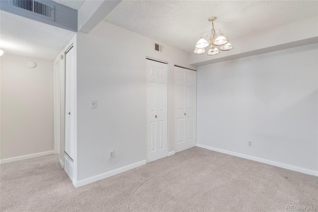12053 E Harvard Ave Unit 107, Aurora, CO 80014 - unfurnished bedroom featuring a textured ceiling, a chandelier, carpet floors, two closets, and baseboards