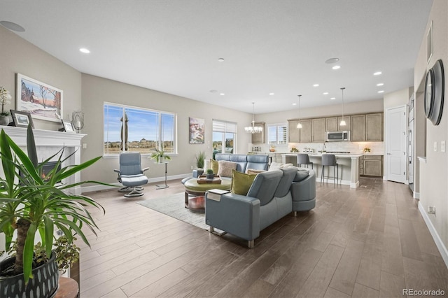 living area featuring dark wood finished floors, baseboards, recessed lighting, a chandelier, and a warm lit fireplace