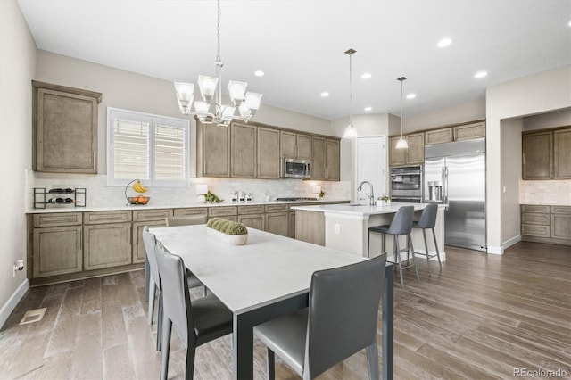 kitchen with recessed lighting, an inviting chandelier, backsplash, stainless steel appliances, and an island with sink