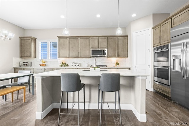 kitchen featuring appliances with stainless steel finishes, tasteful backsplash, a center island with sink, a kitchen bar, and light countertops