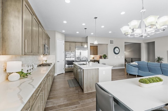 kitchen featuring appliances with stainless steel finishes, an island with sink, dark wood-style floors, open floor plan, and a sink