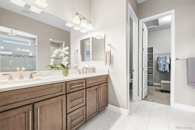 bathroom featuring a marble finish shower, baseboards, double vanity, and a sink