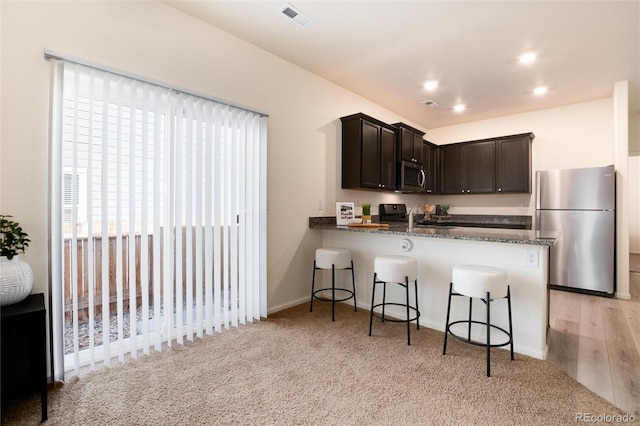 kitchen with visible vents, a breakfast bar area, stainless steel appliances, dark brown cabinets, and a sink