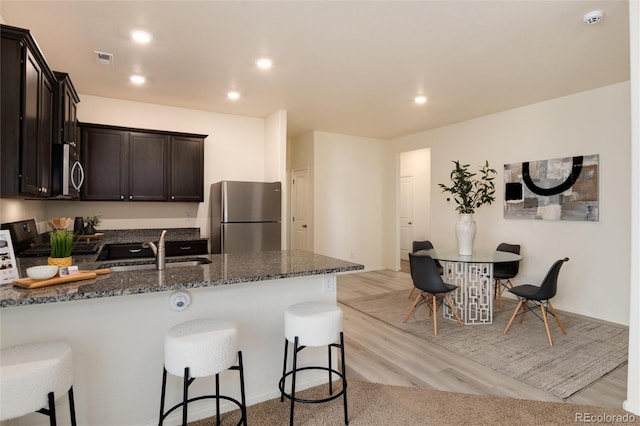 kitchen featuring visible vents, dark stone counters, a peninsula, stainless steel appliances, and a sink