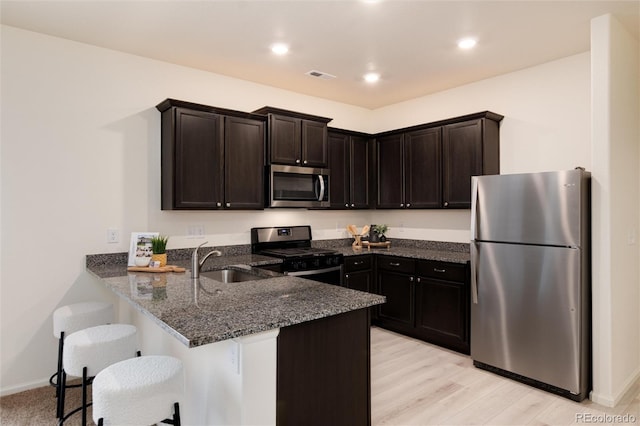 kitchen featuring dark brown cabinetry, dark stone countertops, a peninsula, stainless steel appliances, and a sink