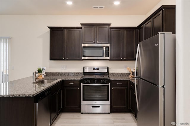 kitchen with a peninsula, a sink, visible vents, appliances with stainless steel finishes, and dark stone counters