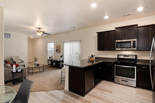 kitchen featuring stainless steel appliances, visible vents, open floor plan, a sink, and dark stone countertops