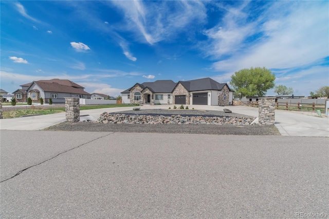 french country inspired facade with concrete driveway, a garage, stone siding, fence, and a residential view