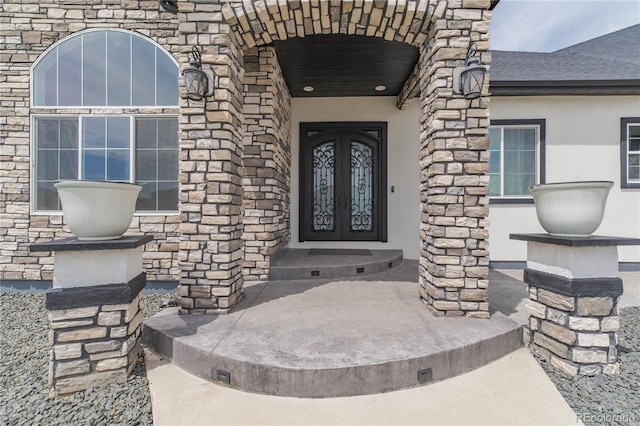 property entrance featuring stone siding, stucco siding, and french doors