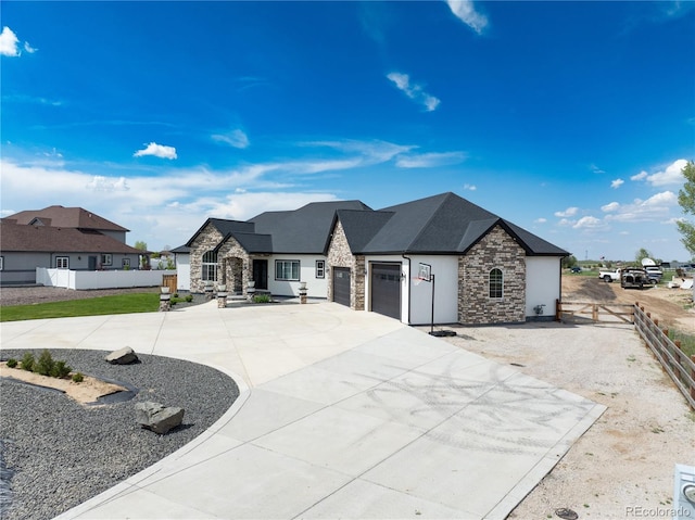 french country home with stone siding, driveway, stucco siding, a garage, and fence