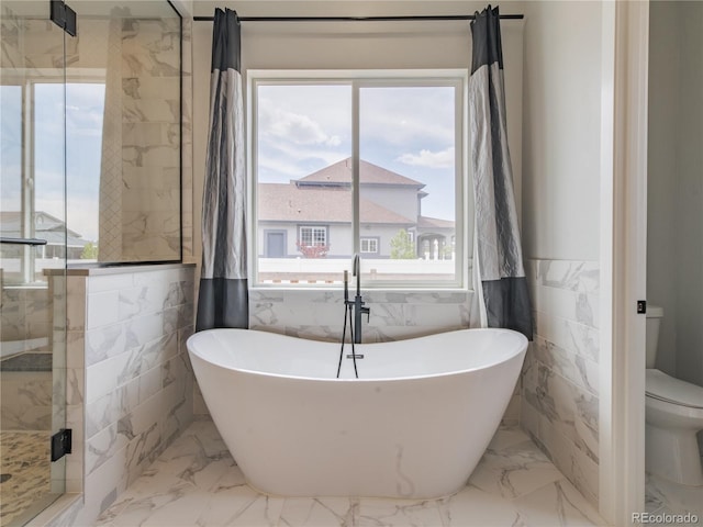 full bath with tile walls, a shower stall, a soaking tub, toilet, and marble finish floors