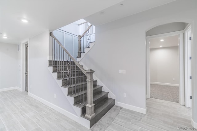 stairs with arched walkways, baseboards, wood finished floors, and recessed lighting