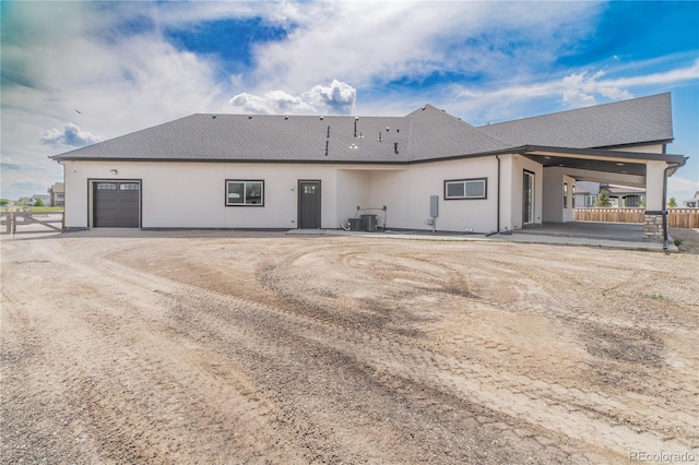 rear view of house featuring fence, a garage, and stucco siding