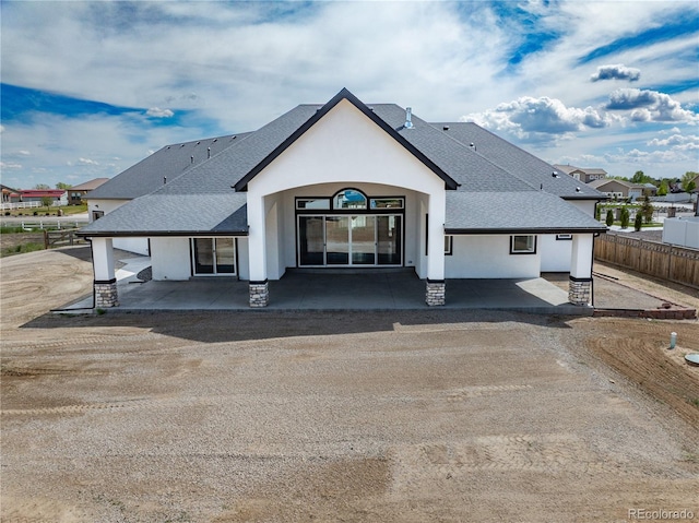 rear view of property with roof with shingles, fence, and stucco siding
