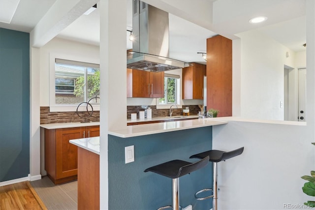 kitchen with light countertops, brown cabinets, light wood finished floors, island exhaust hood, and a breakfast bar area