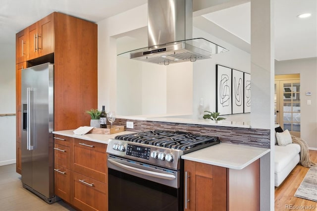 kitchen with island exhaust hood, light countertops, brown cabinets, appliances with stainless steel finishes, and light wood finished floors