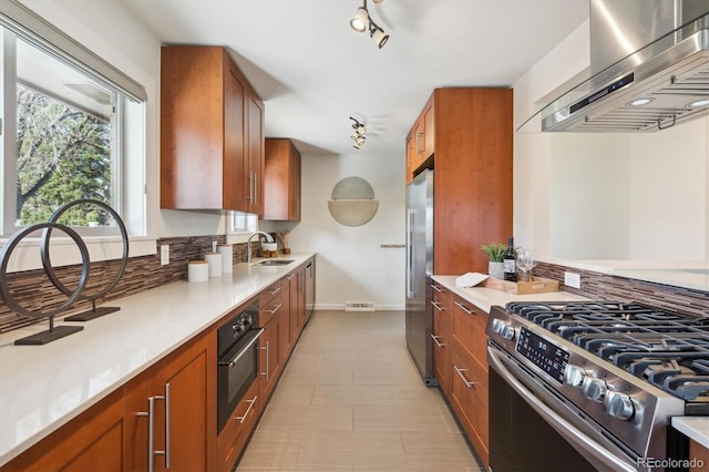 kitchen featuring brown cabinets, ventilation hood, rail lighting, and stainless steel appliances