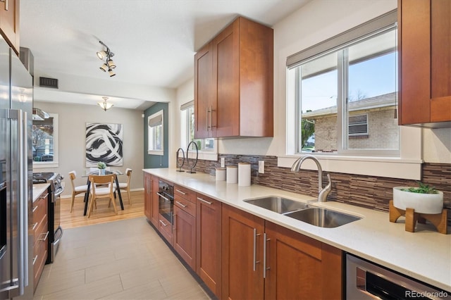 kitchen with light countertops, backsplash, brown cabinetry, stainless steel appliances, and a sink