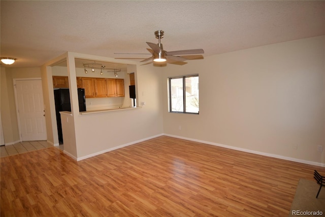 unfurnished living room featuring ceiling fan, light hardwood / wood-style flooring, and a textured ceiling