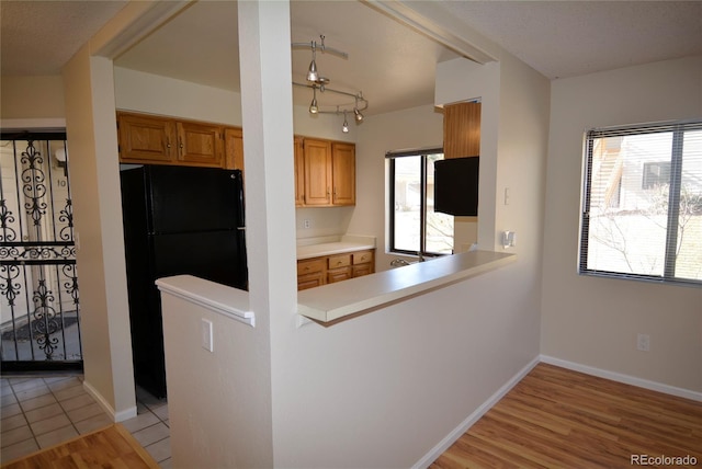 kitchen with a healthy amount of sunlight, black refrigerator, kitchen peninsula, and light hardwood / wood-style flooring