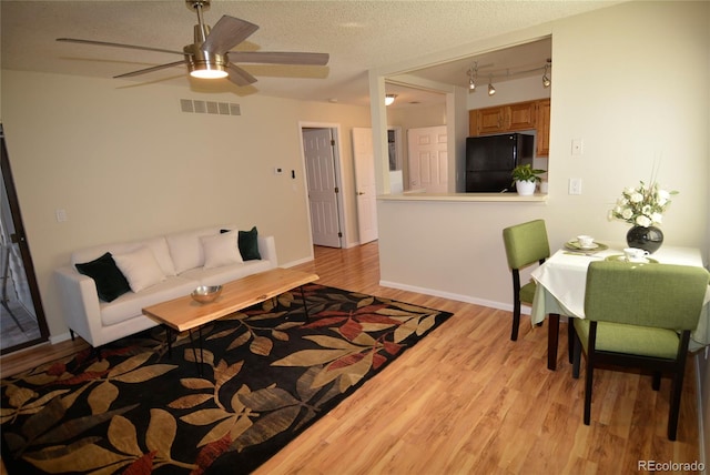 living room featuring light wood finished floors, baseboards, visible vents, and a textured ceiling