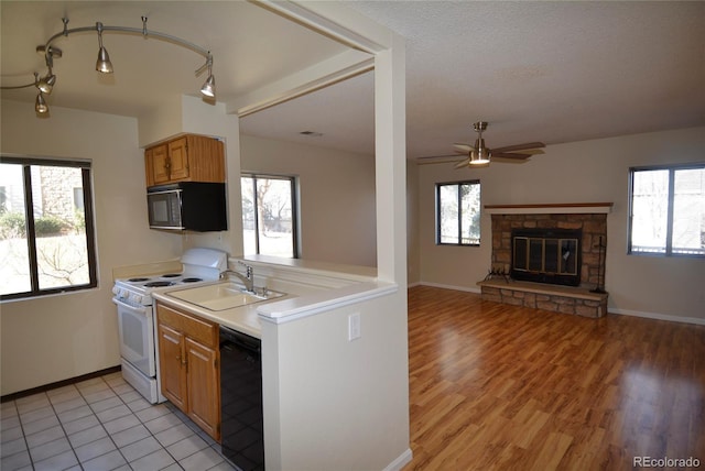 kitchen featuring a fireplace, light countertops, a ceiling fan, a sink, and black appliances