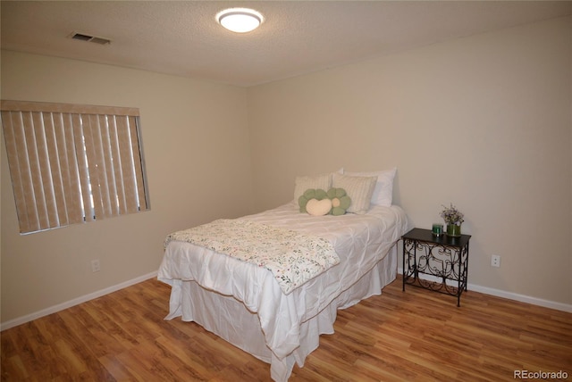 bedroom featuring visible vents, a textured ceiling, baseboards, and wood finished floors