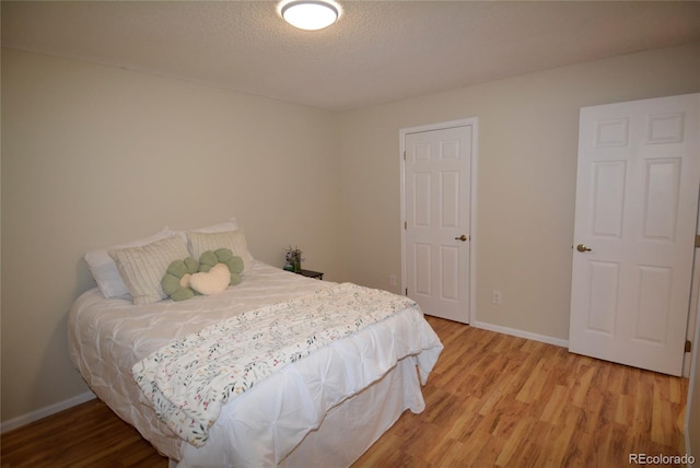 bedroom with light wood finished floors, baseboards, and a textured ceiling