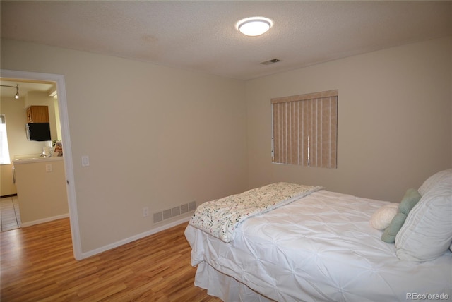 bedroom with a textured ceiling, light wood finished floors, visible vents, and baseboards