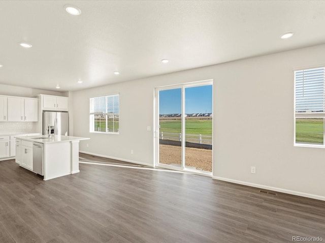 kitchen with white cabinets, stainless steel appliances, dark wood-type flooring, and an island with sink