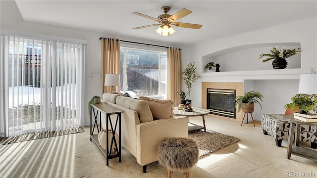 living room with a tiled fireplace, light colored carpet, and ceiling fan