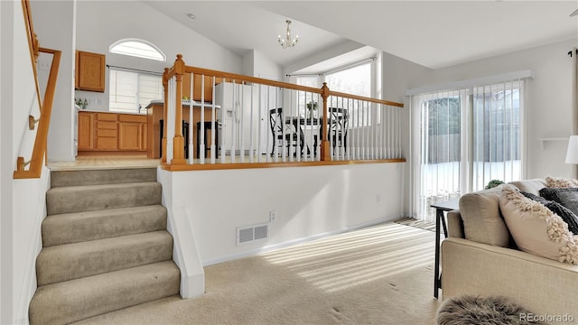 staircase featuring an inviting chandelier, a healthy amount of sunlight, vaulted ceiling, and carpet floors